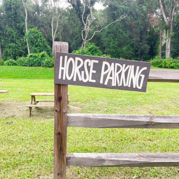 A "HORSE PARKING" sign on a wooden fence in a grassy field with trees.