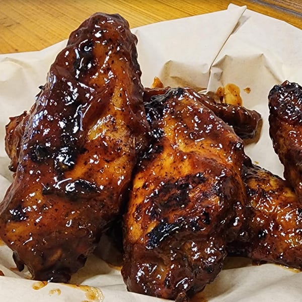 Close-up of Pudgee's Eatery and Market's glistening, saucy chicken wings served in a paper-lined basket.