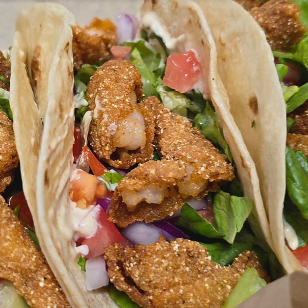 Close-up of Pudgee's Eatery and Market's fried shrimp tacos with lettuce, tomatoes, and onions.