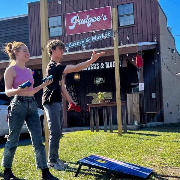 Two people playing cornhole on a sunny day outside Pudgee's Eatery & Market.